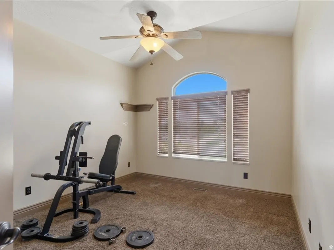 Carpeted room featuring a ceiling fan with integrated lighting, a large arched window with horizontal blinds, and a decorative corner shelf