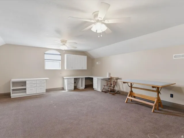 Spacious room featuring carpeting, two ceiling fans, built-in white cabinetry, a built-in white desk with drawers, and an arched window