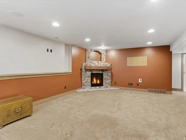 Spacious interior featuring a corner stone-clad fireplace with a rustic wood mantel, carpeted flooring, recessed lighting, and a two-tone wall treatment