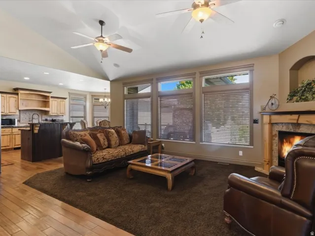 Living area featuring a stone surround fireplace with wood mantel, vaulted ceilings, and ceiling fans with light fixtures