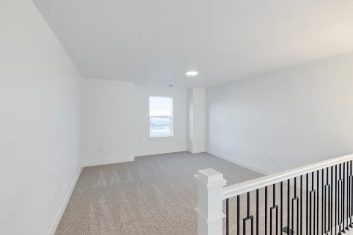 Carpeted loft space featuring a white spindle railing with black balusters, a recessed ceiling light, and a window