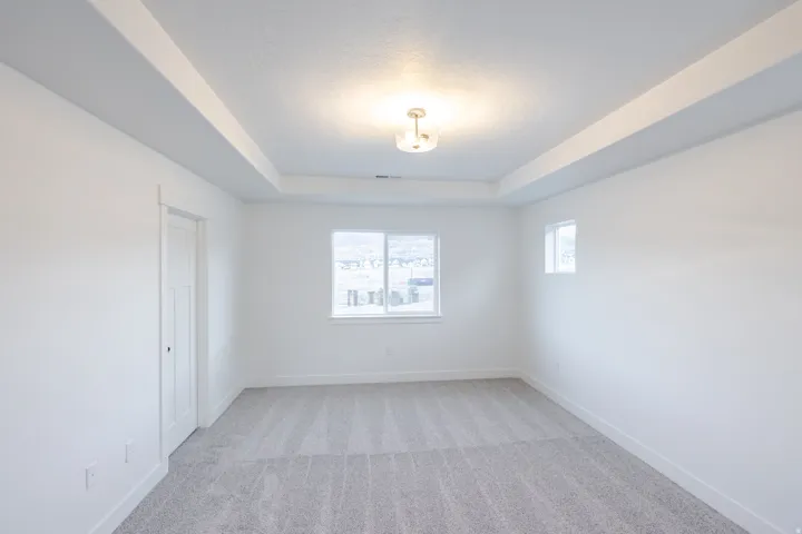 Recessed ceiling with central light fixture, two windows providing natural light, white trim, and gray carpeting