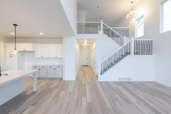 Open concept living area with wood-finish flooring, a grand staircase featuring black metal spindles, and a kitchen island with a white countertop