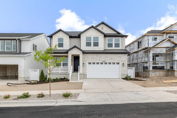 Two-story residence with a stone and siding exterior, front porch with white railings, attached two-car garage, and a concrete driveway