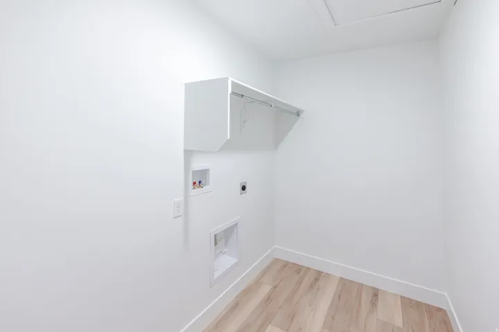 Bright utility space featuring wood-finish flooring, white walls, and built-in upper cabinetry with an integrated hanging rod