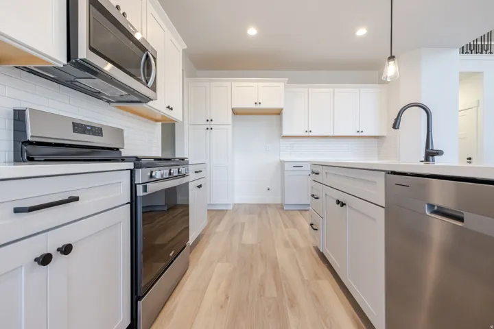 Kitchen with light wood-finish flooring, white cabinetry, stainless steel appliances, white subway tile backsplash, and a central island with a matte black faucet