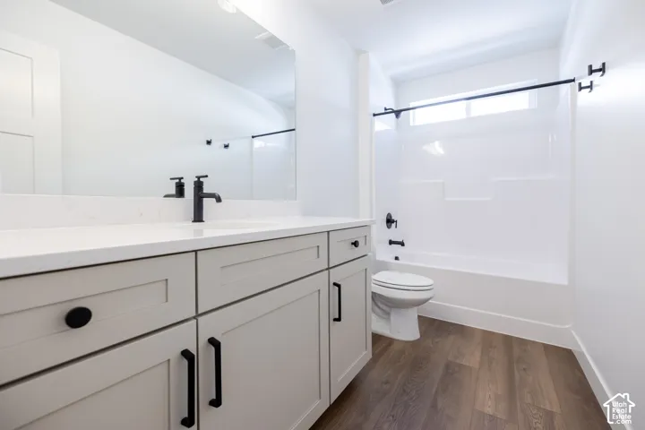 Modern bathroom featuring a white shaker-style vanity with dual sinks, white quartz countertop, matte black hardware and faucet, frameless glass shower enclosure with chrome fixtures, wood-finish flooring, and abundant natural light from the window