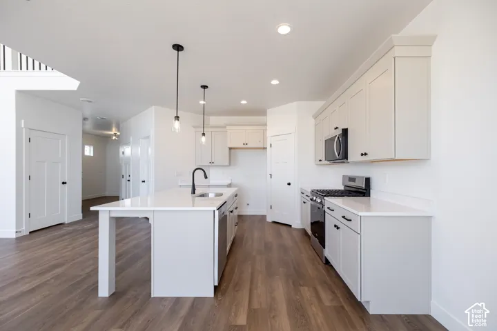 Kitchen with wood-finish flooring, an island with pendant lighting, white cabinetry, integrated stainless steel appliances, and solid surface countertops
