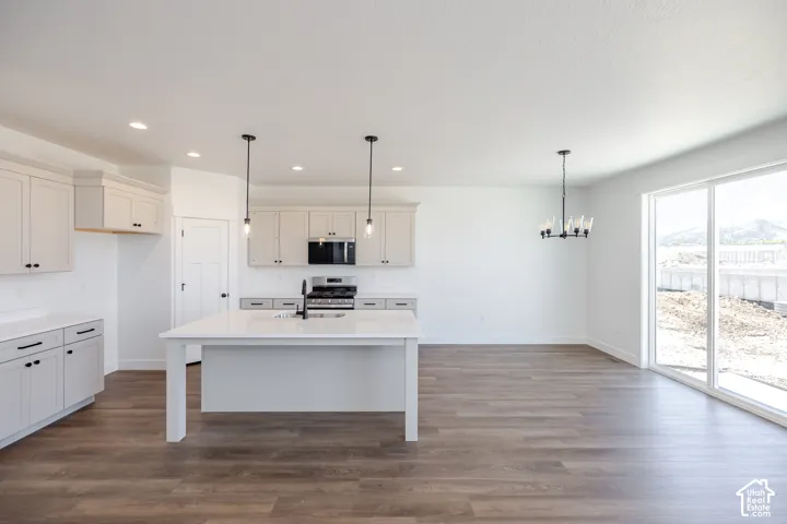 Open-concept kitchen and dining area featuring white cabinetry, stainless steel appliances, a large center island with white base, pendant lighting, wood-finish flooring throughout, and expansive glass sliding doors providing natural light