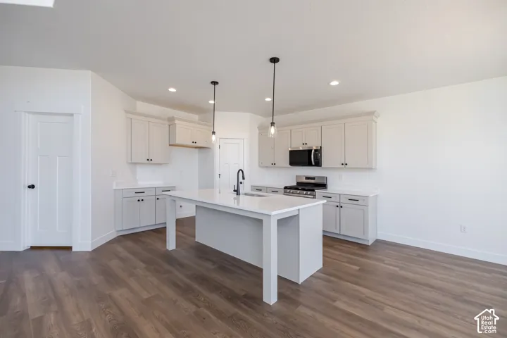 Kitchen featuring wood-finish flooring, white cabinetry with dark hardware, white countertops, a central island with a sink, and pendant lighting