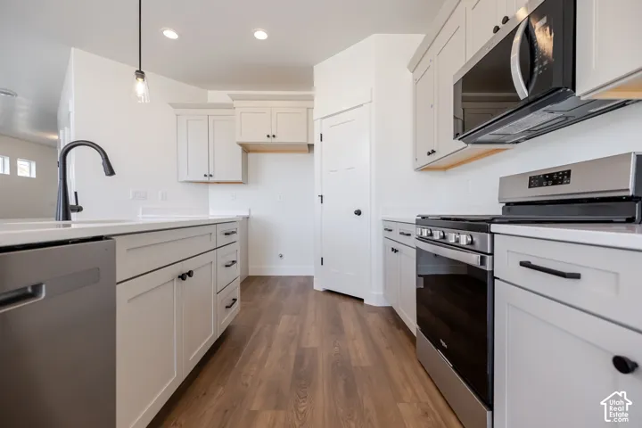 Modern galley kitchen featuring white cabinetry with hardware accents, wood-finish flooring, stainless steel appliances including dual ovens and a gas cooktop, quartz countertops, and a contemporary black gooseneck faucet at the sink