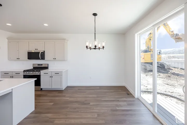 Modern kitchen and dining area featuring white cabinetry with hardware accents, stainless steel appliances including a gas range and microwave, white quartz countertops, a center island with seating, wood-finish flooring throughout, recessed ceiling light