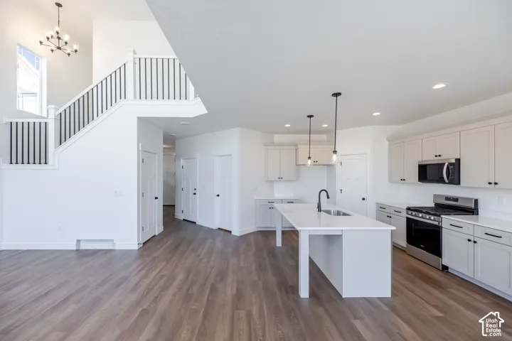 Open-concept living area featuring wood-finish flooring, a contemporary kitchen island with a sink, stainless steel appliances, and a two-story staircase with a modern chandelier