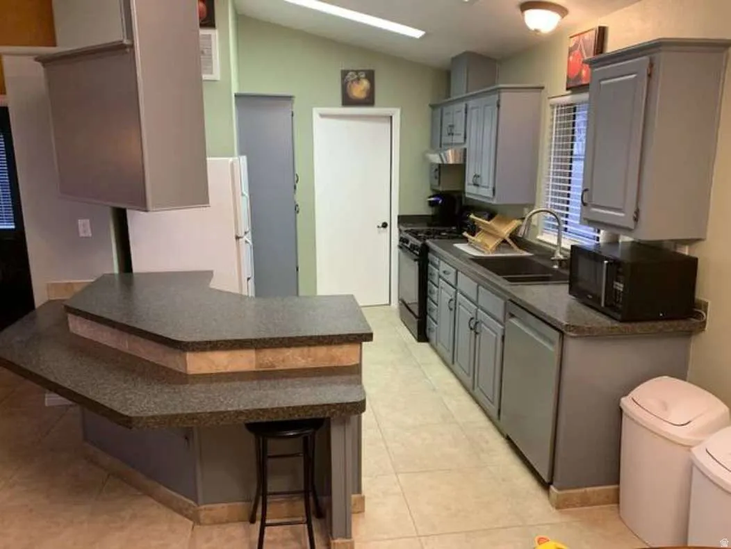 Kitchen with gray cabinets, black appliances, a kitchen bar, lofted ceiling, and a peninsula