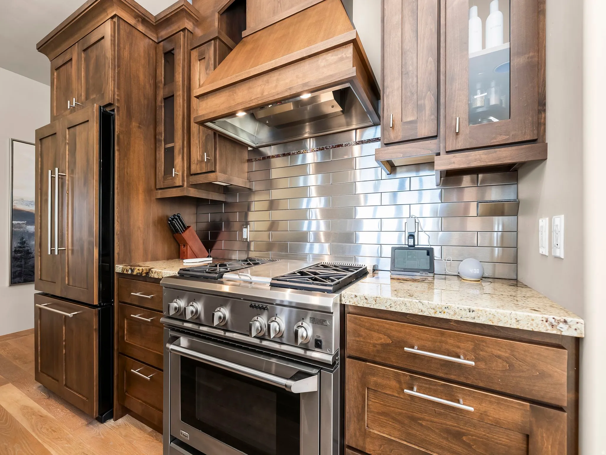Kitchen with glass fronted cabinets, high quality appliances, light stone counters, light wood-style flooring, and decorative backsplash