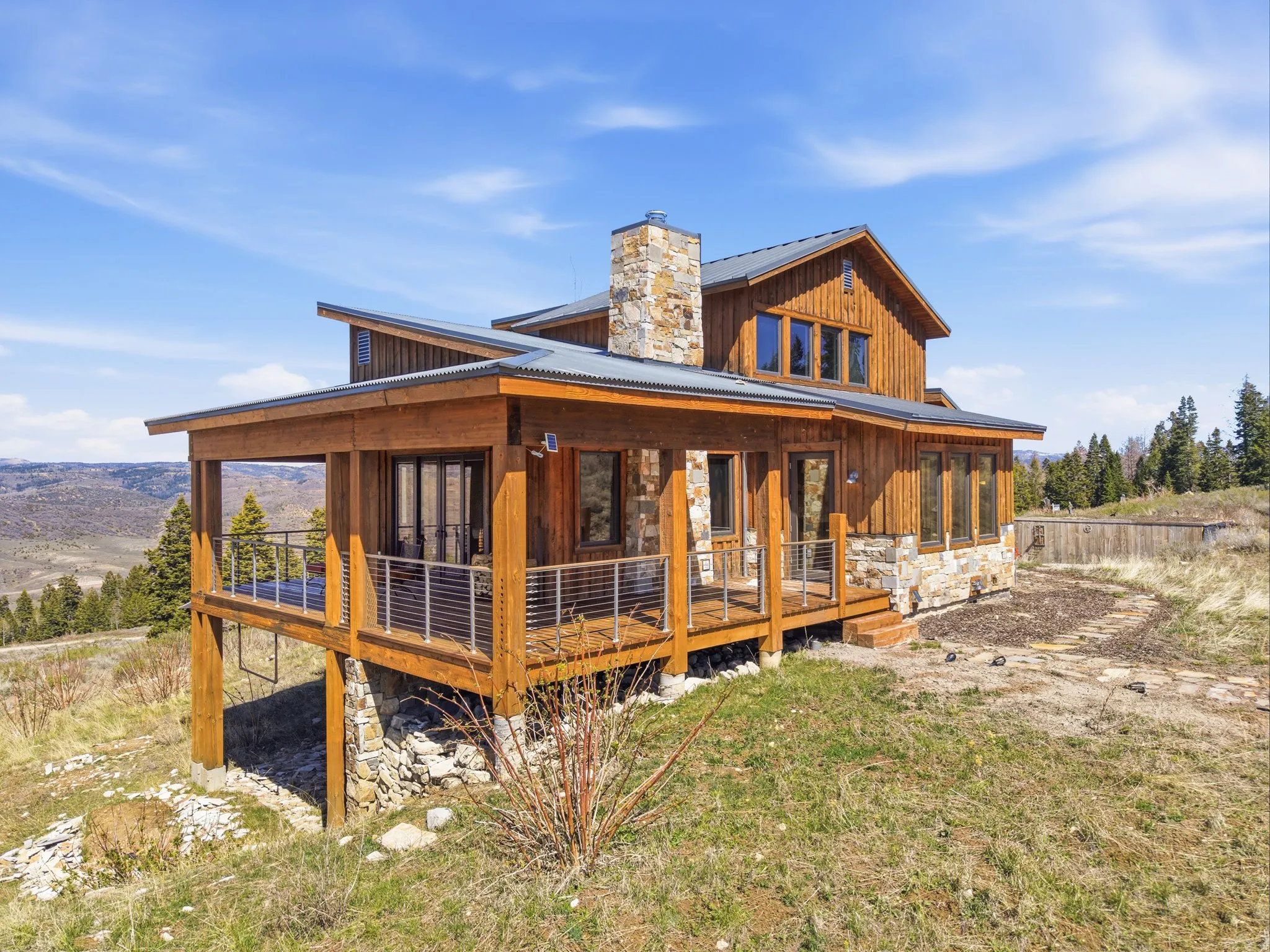 Rear view of property with a chimney, a porch, stone siding, board and batten siding, and a metal roof