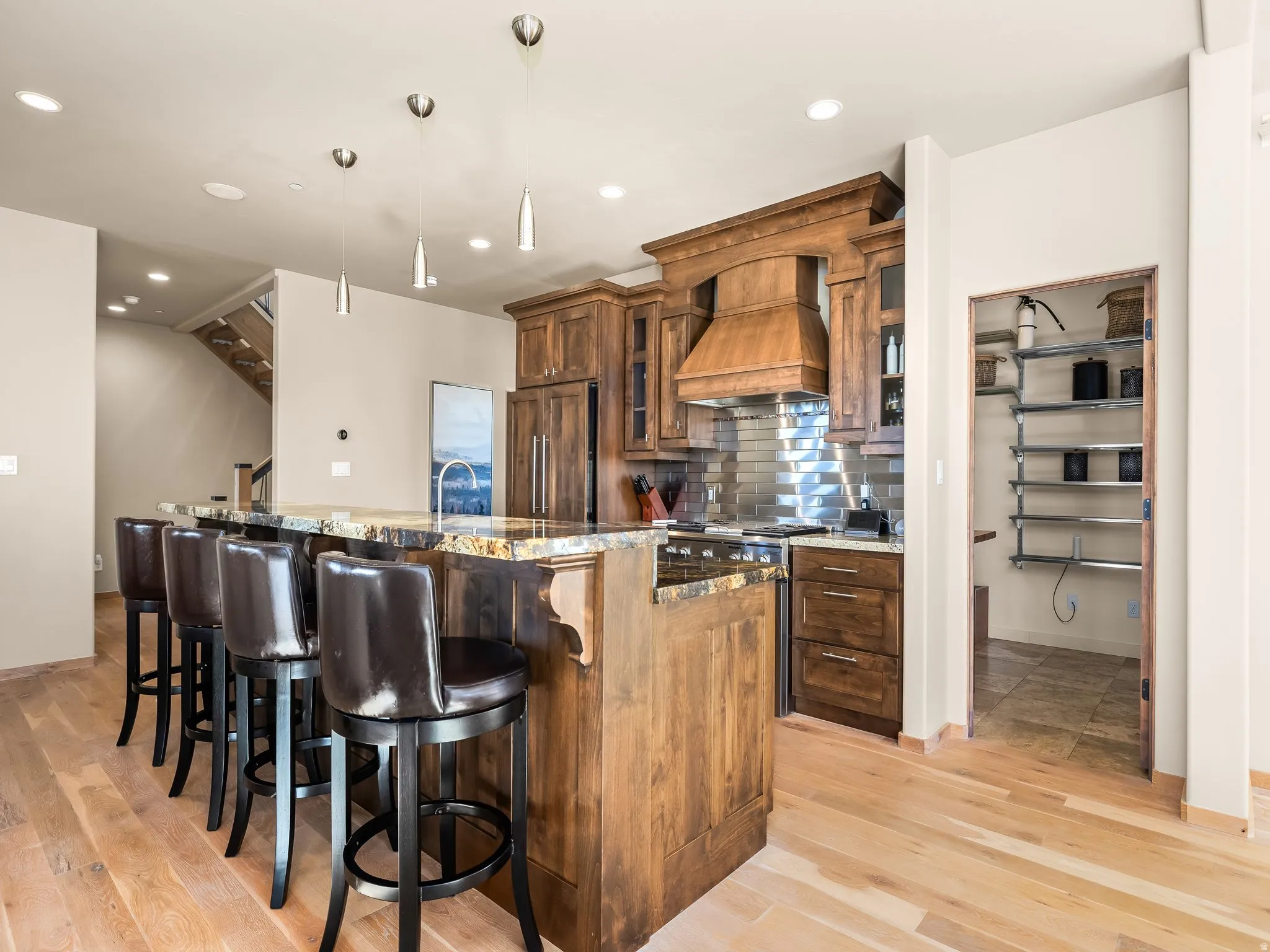 Kitchen with dark stone counters, a kitchen bar, wood finish cabinets, light wood-style flooring, and glass insert cabinets