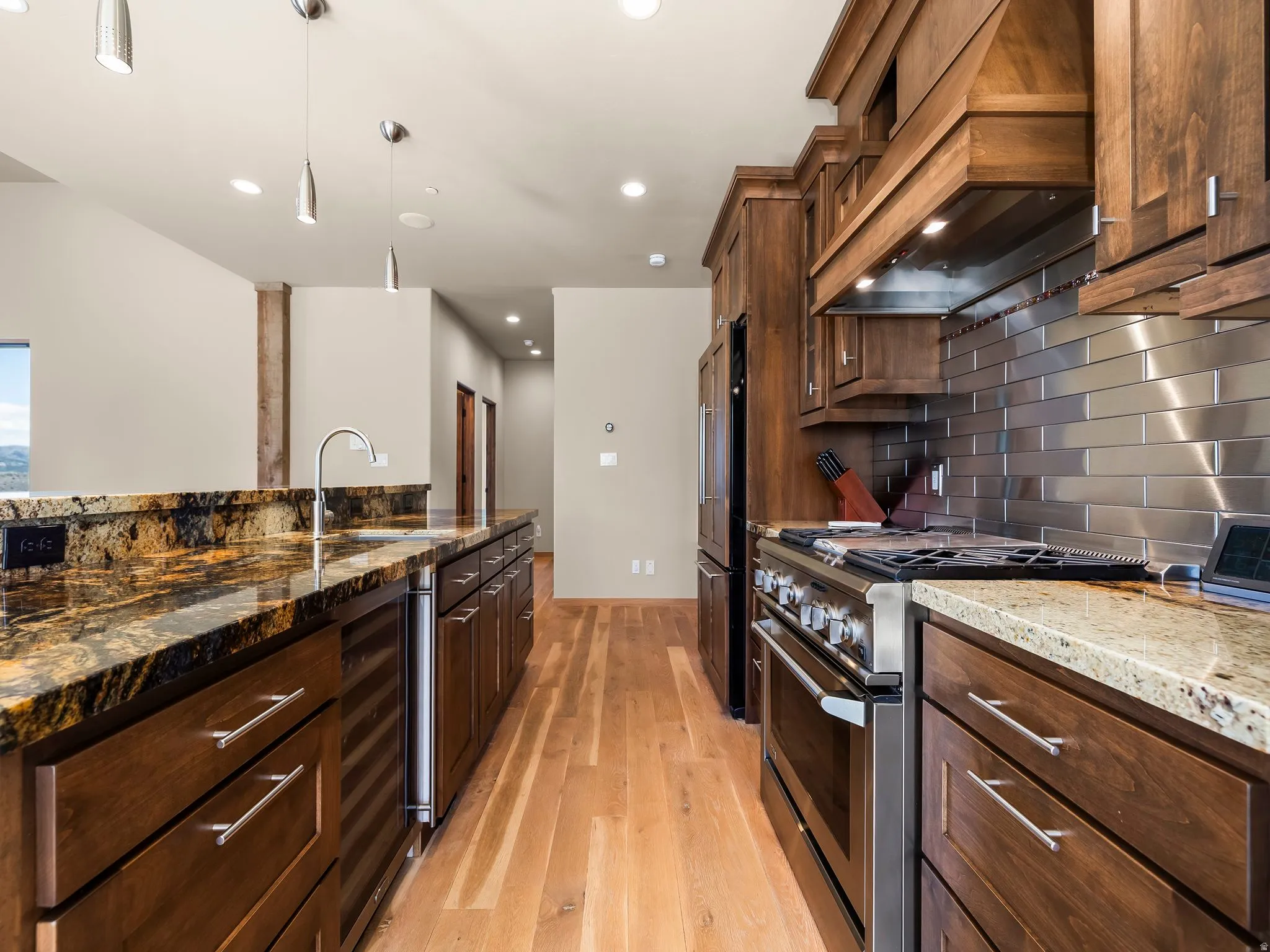 Kitchen featuring dark stone counters, stainless steel appliances, light wood-style flooring, beverage cooler, and hanging light fixtures