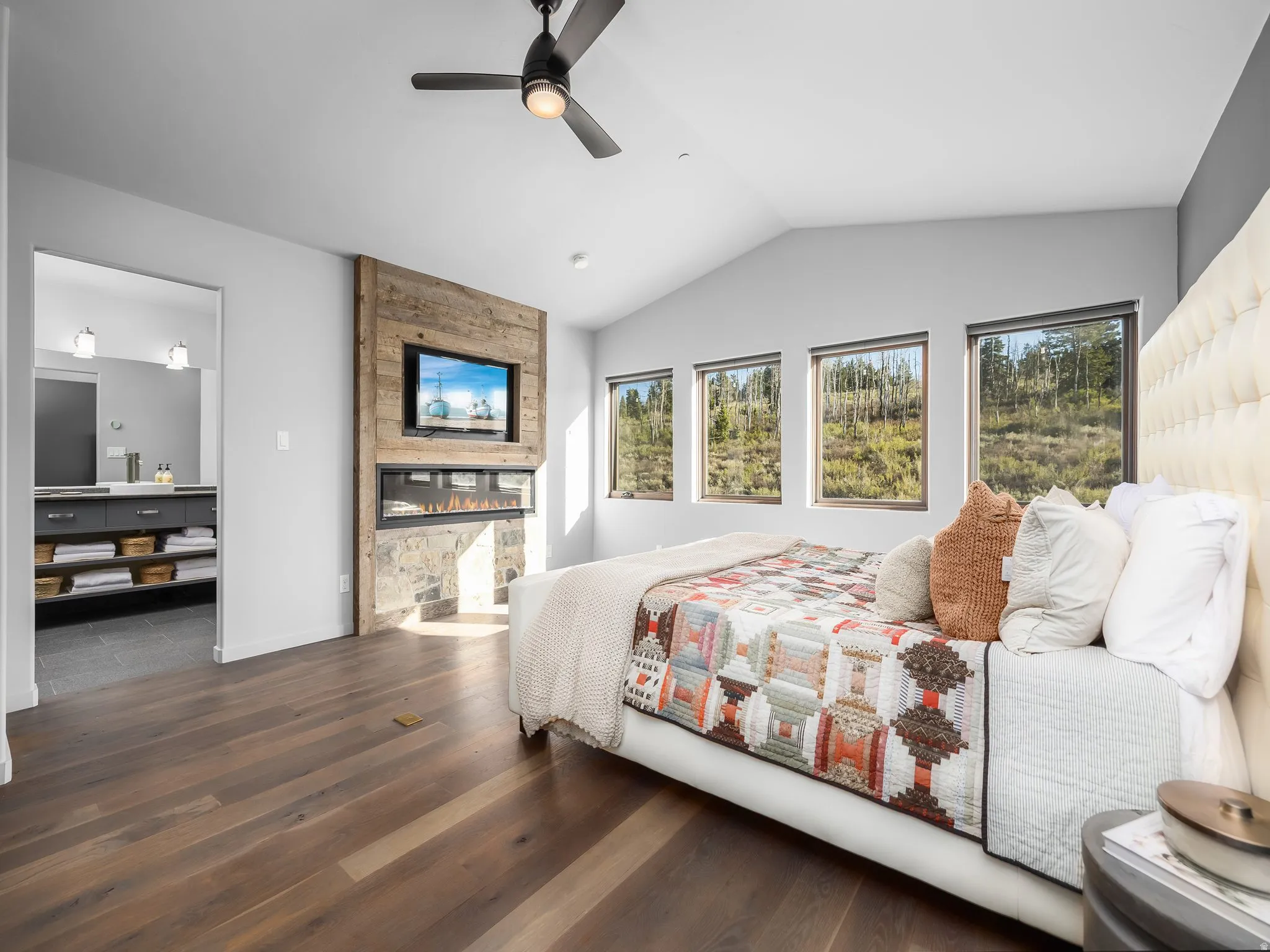 Bedroom featuring multiple windows, dark wood-style floors, a large fireplace, vaulted ceiling, and a ceiling fan