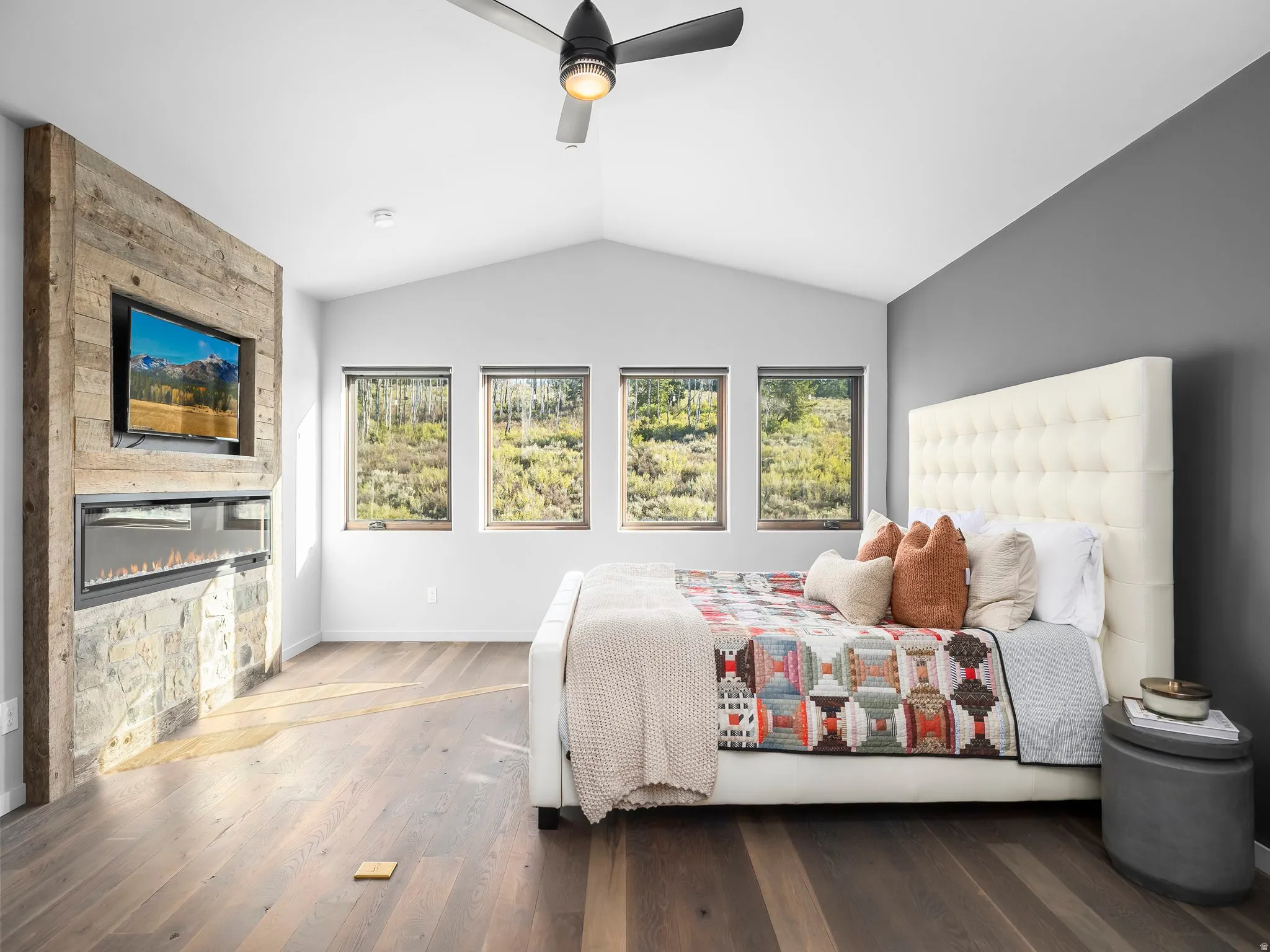 Bedroom featuring multiple windows, wood finished floors, ceiling fan, and a large fireplace