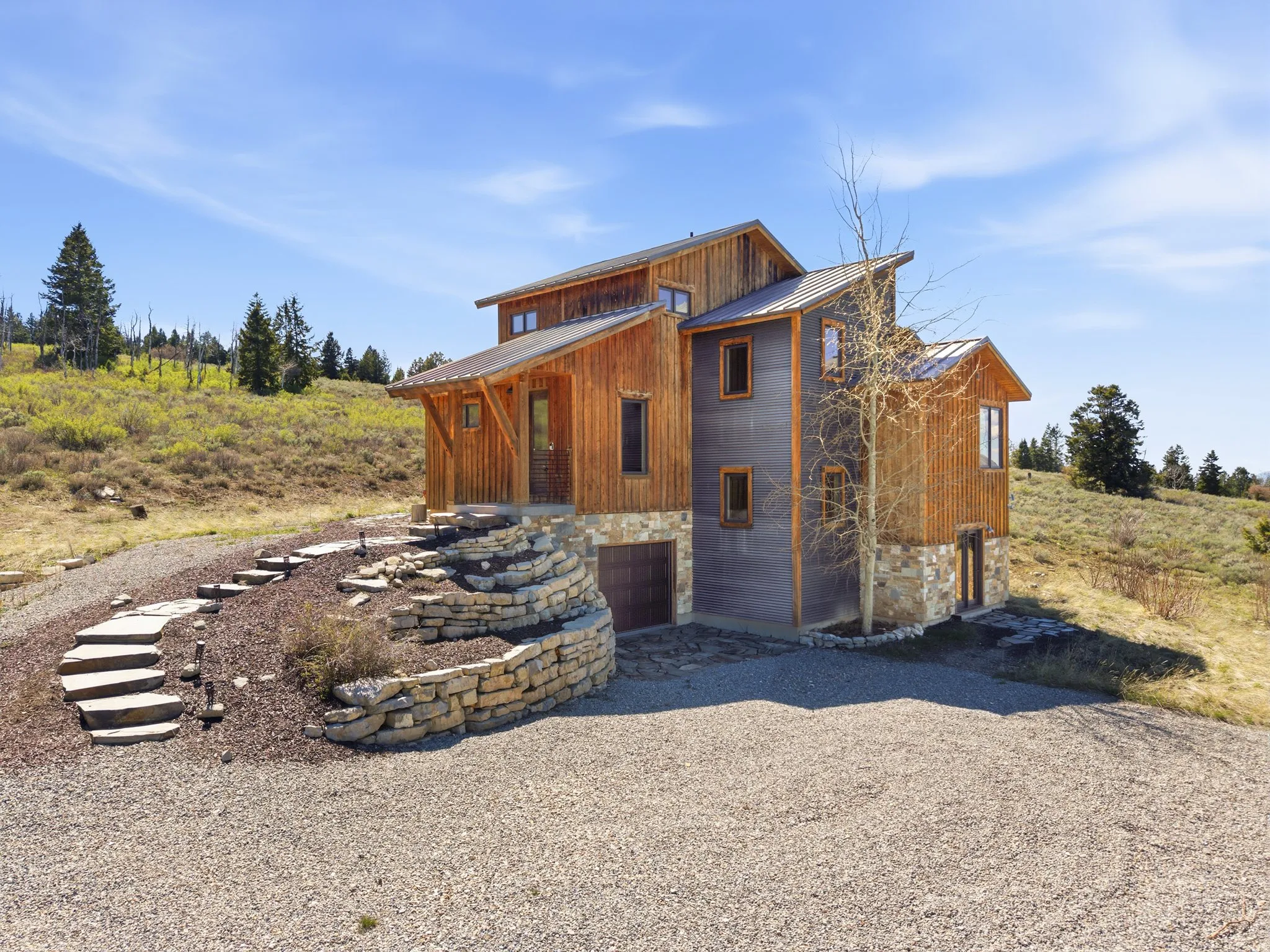 Rear view of house with an attached garage, stone siding, driveway, and a standing seam roof