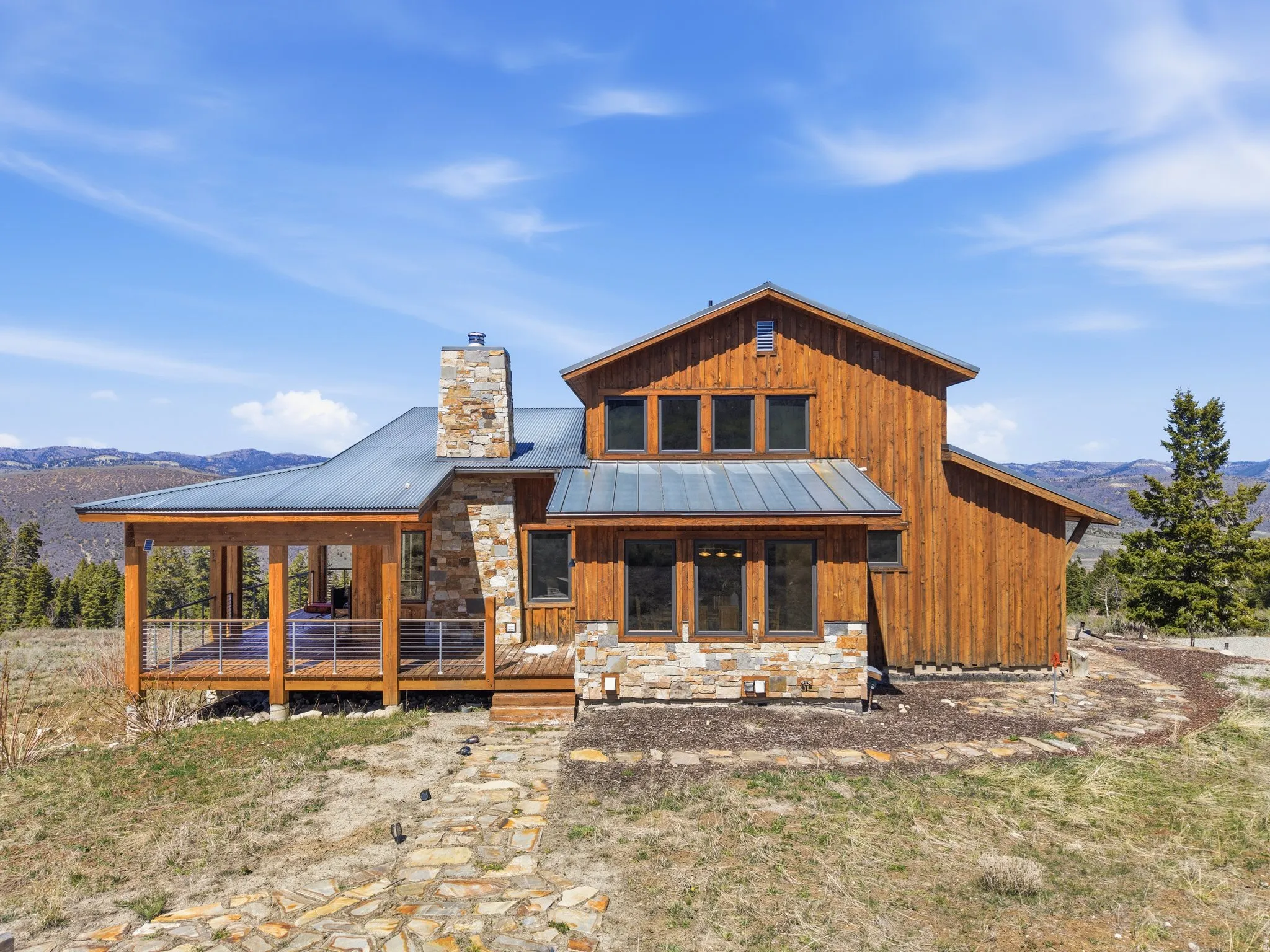 Rear view of property featuring a standing seam roof, stone siding, a deck with mountain view, and board and batten siding