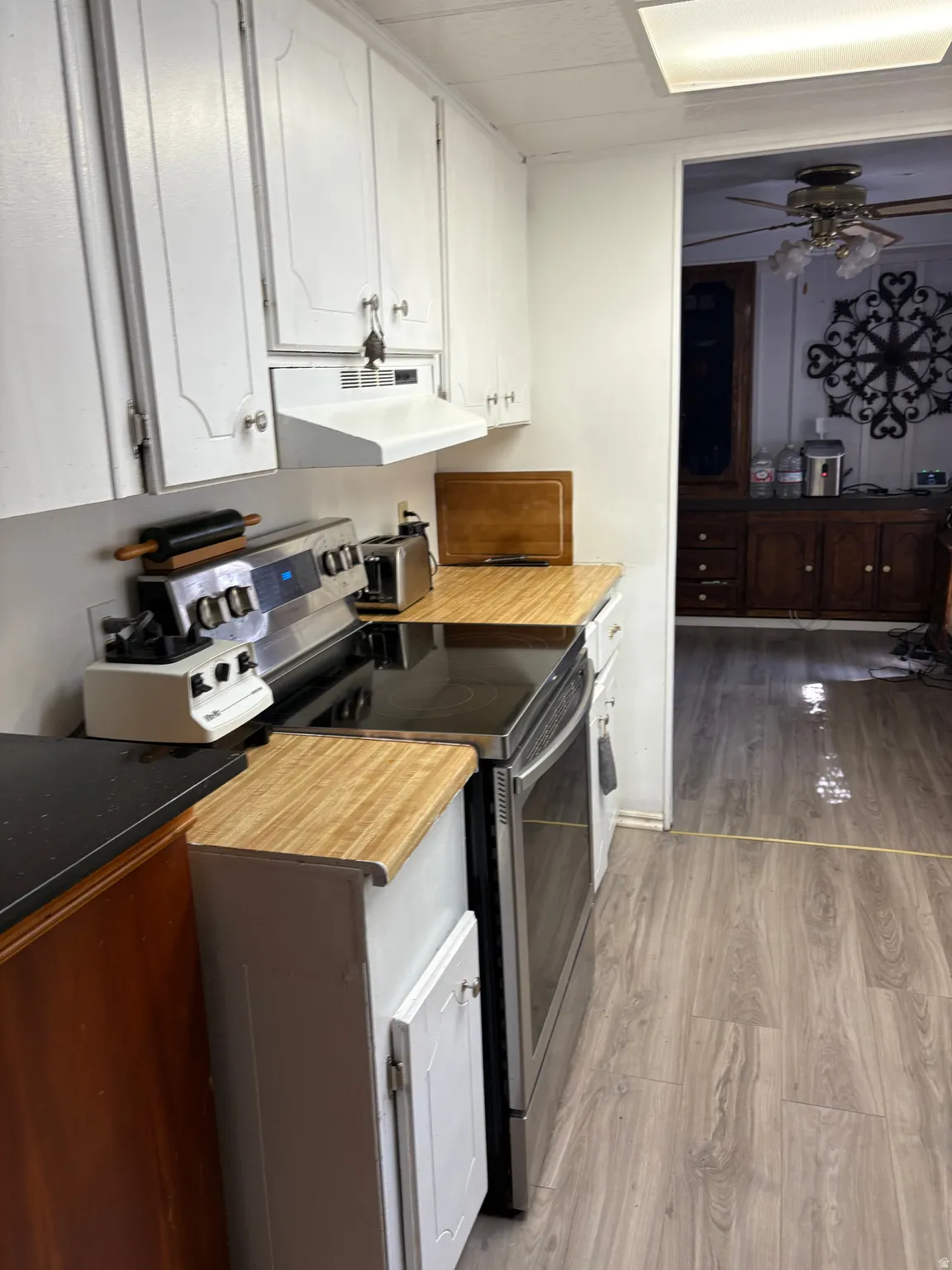 Kitchen with stainless steel electric range, light wood finished floors, ceiling fan, white cabinets, and range hood