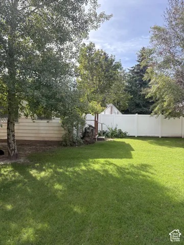 Expansive lawn area, mature trees, white privacy fencing, and wood-sided exterior