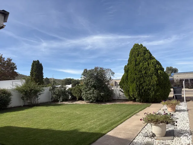 Expansive outdoor space featuring a manicured lawn, established landscaping, white privacy fencing, and a concrete paver path with decorative white gravel