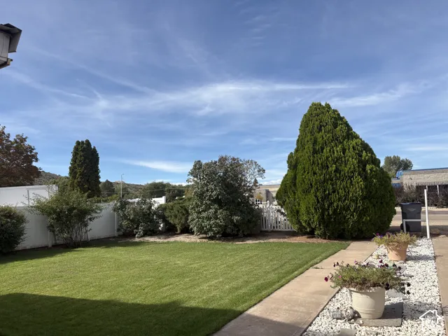 Expansive backyard featuring a manicured lawn, white privacy fencing, and mature landscaping
