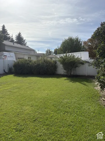 Expansive backyard featuring a manicured lawn, established shrubs, and privacy fencing
