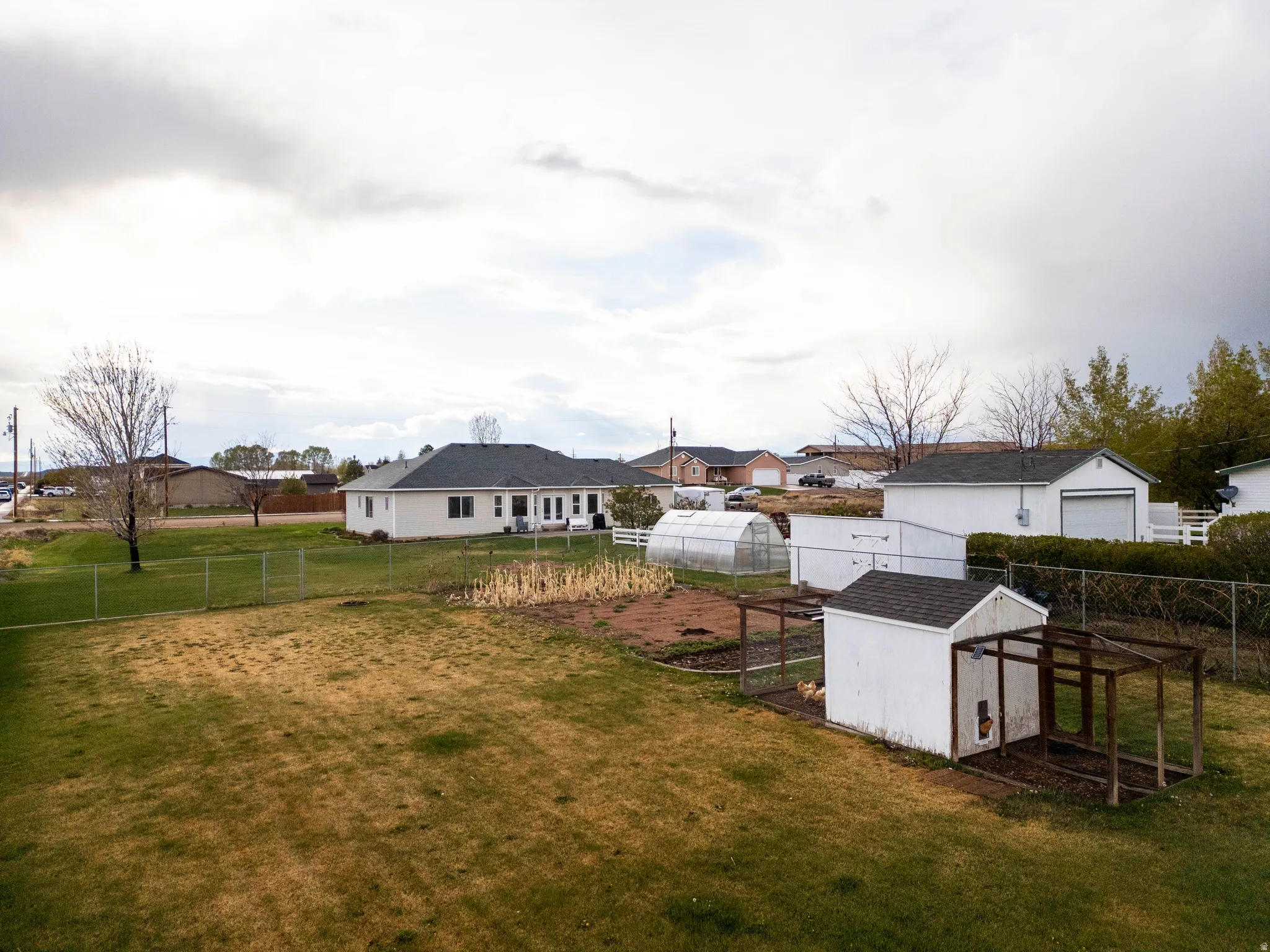 Fenced backyard with an outbuilding, a greenhouse, a residential view, and exterior structure
