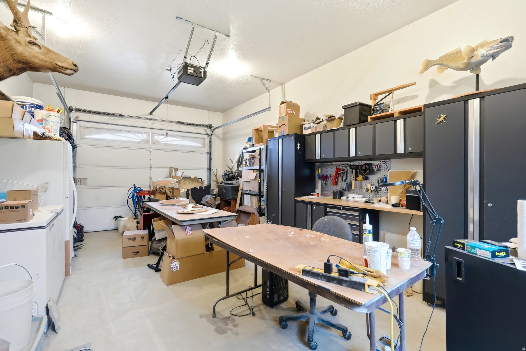 Garage featuring white refrigerator, freestanding refrigerator, and a garage door opener