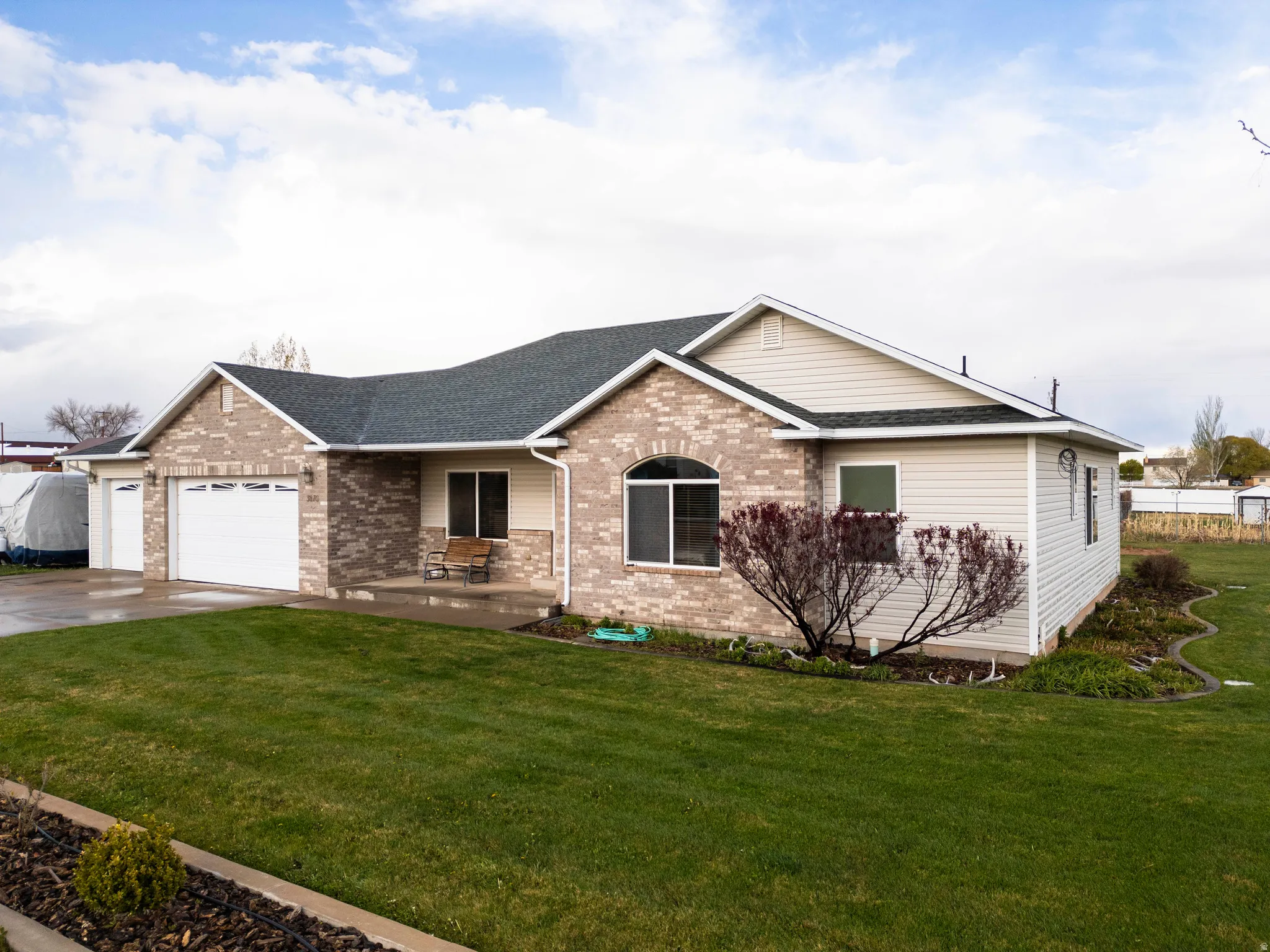 Ranch-style house with a shingled roof, brick siding, a garage, a front lawn, and covered porch