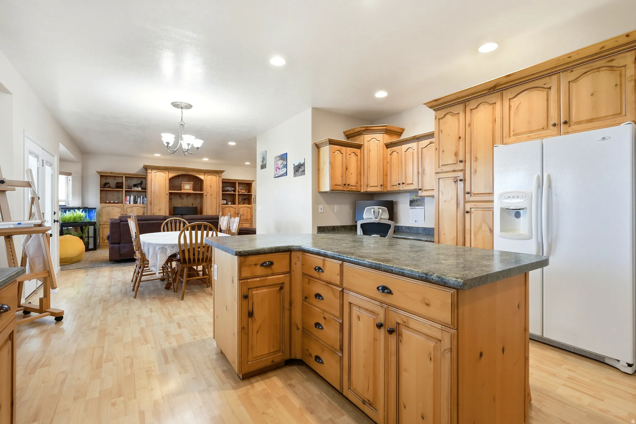 Kitchen with white fridge with ice dispenser, dark countertops, a chandelier, and light wood-style floors