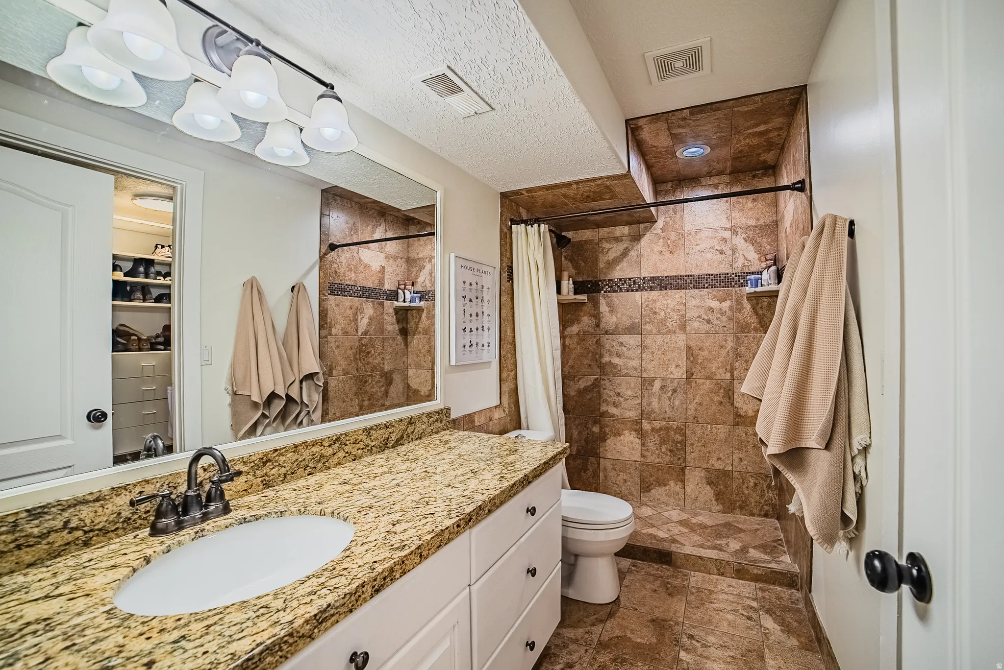Full bath with a stall shower, vanity, a textured ceiling, and dark stone finish flooring