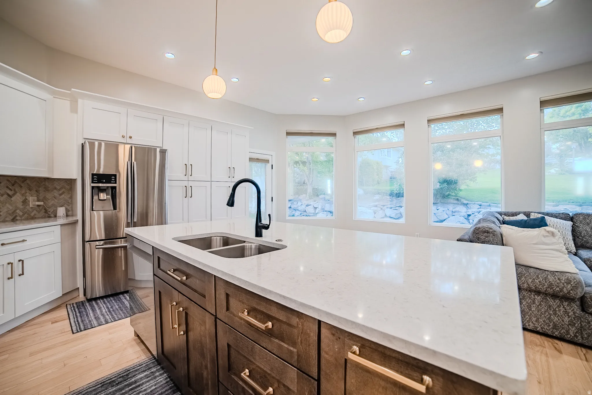 Kitchen featuring stainless steel appliances, dual tone cabinets, open floor plan, light stone countertops, and light wood-type flooring