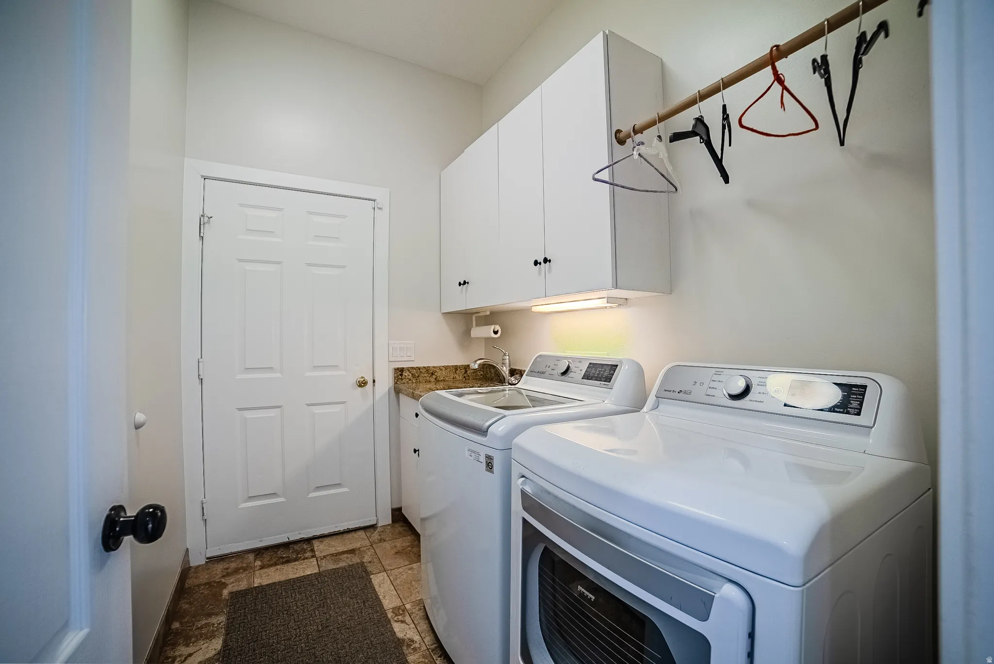 Laundry area with washer and clothes dryer, stone finish floors, and cabinet space