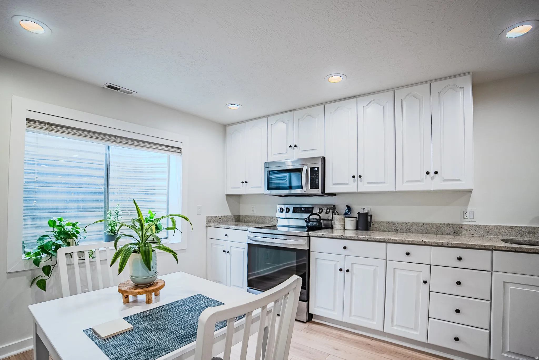 Kitchen featuring light stone countertops, stainless steel appliances, white cabinets, light wood finished floors, and recessed lighting