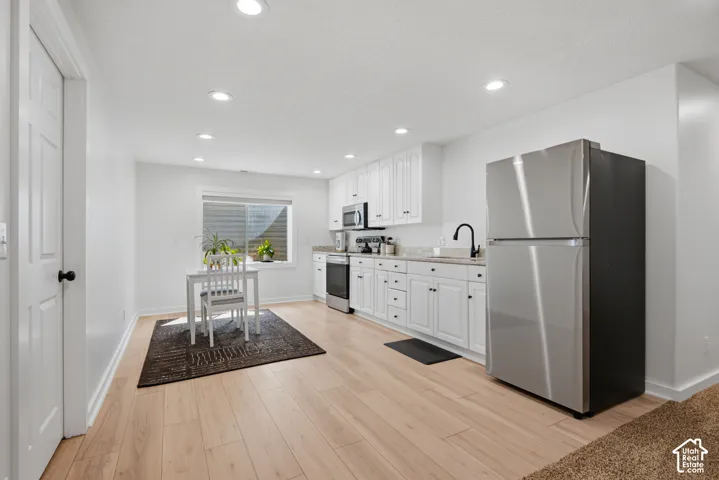 Full kitchen featuring white cabinetry, stainless steel appliances, light-toned wood-finish flooring, and recessed lighting