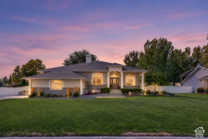 Single-story residence featuring a stucco exterior, arched window detailing, covered entryway with columns, stone masonry accents, and a wide-span front lawn