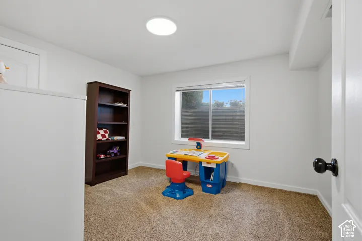 Recessed ceiling lighting, white painted walls, window with white trim, tan carpet flooring, and a white door with a black doorknob