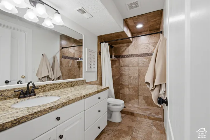 Granite-finish countertop with an undermount sink, white vanity cabinetry with dark hardware, a tiled shower with an integrated shelf, and recessed lighting