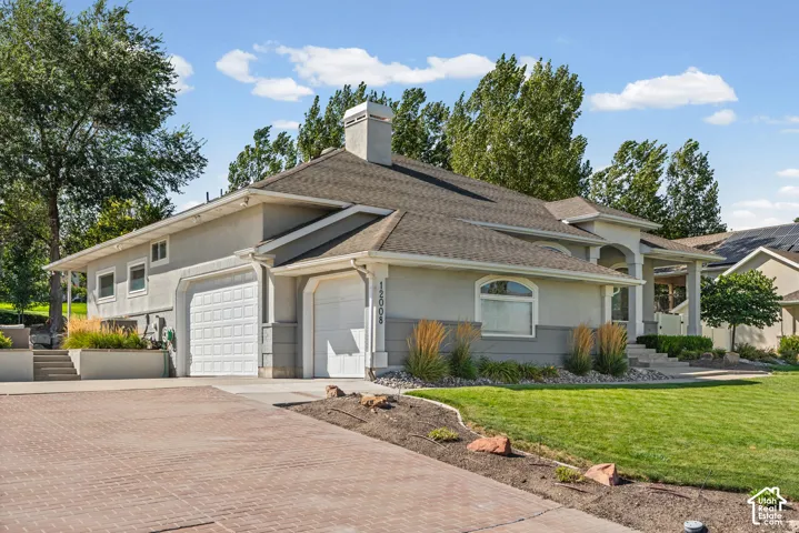 Stucco exterior with a shingled roof, featuring a brick paver driveway, an attached two-car garage, and a covered porch entry