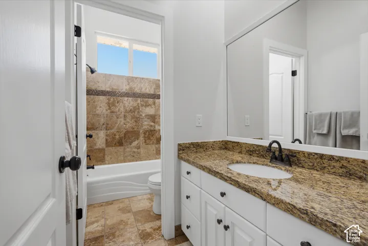 Bathroom featuring a white vanity with a stone countertop, a built-in sink, a large wall mirror, and a shower with tile surround