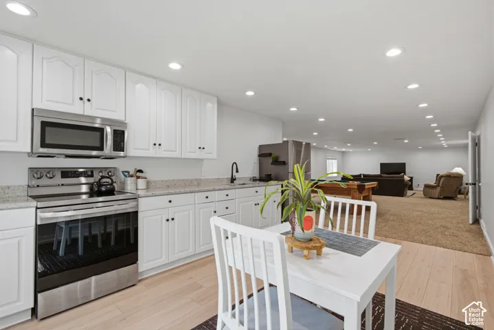 White cabinetry with black hardware, stainless steel appliances, light-toned wood-finish flooring, recessed lighting, and a neutral carpeted area