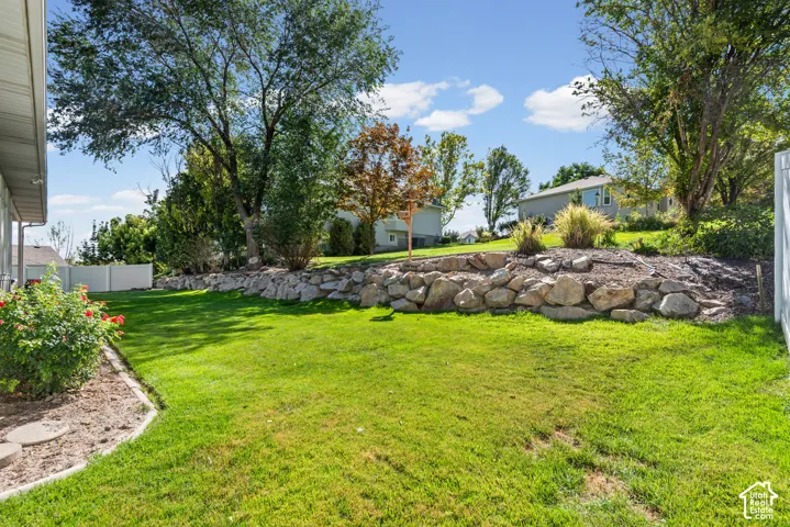 Expansive green lawn with a rock retaining wall, mature trees, and landscaping