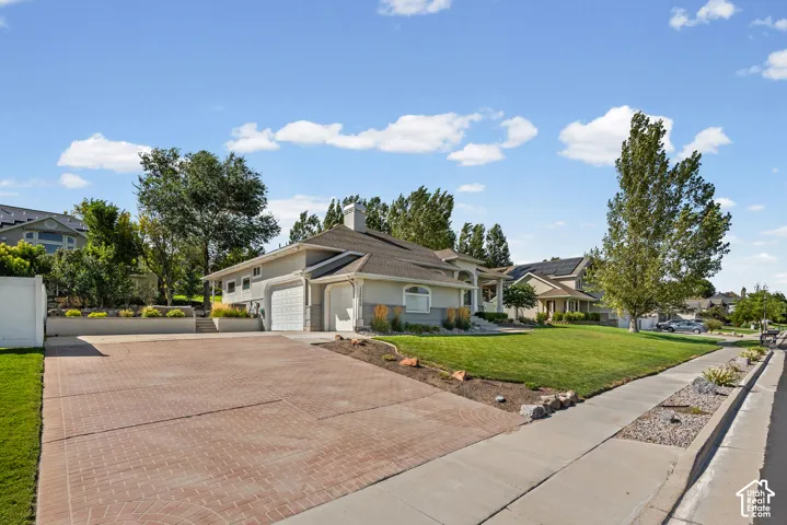 Stucco exterior with stone accents, attached garage, brick-patterned driveway, and a manicured lawn