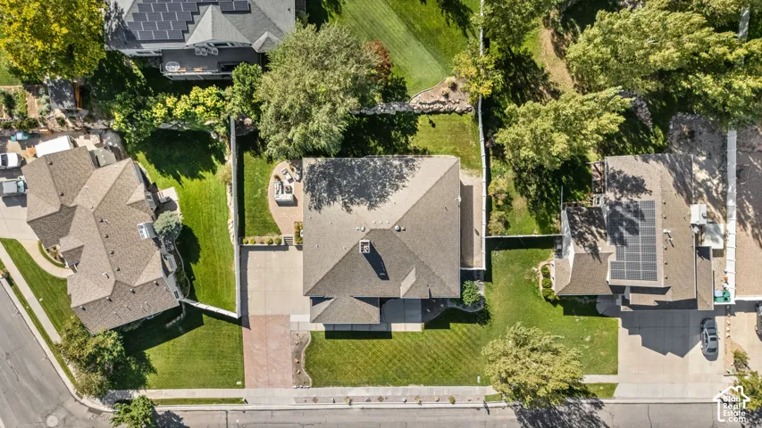 Gabled roof with solar panels, mature trees, manicured lawns, and a paver driveway