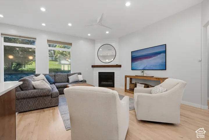 Recessed lighting, light wood-finish flooring, corner fireplace with white tile surround, wooden mantel, and a ceiling fan